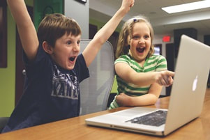 two children cheering in front of a laptop