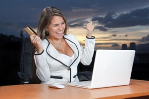 Woman in blazer excitedly holding a credit card in front of a laptop